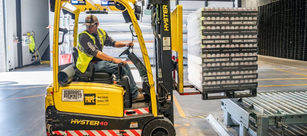 A worker wearing a safety vest and cap operates a yellow forklift following a traffic management plan